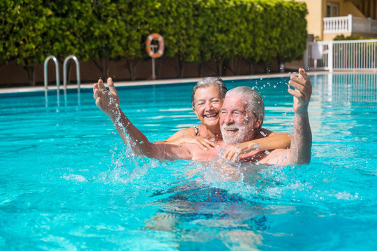 Couple of two happy seniors having fun and enjoying together in the swimming pool smiling and playing. Happy people enjoying summer outdoor in the water

