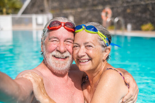 Couple of two happy seniors having fun and enjoying together in the swimming pool taking a selfie picture smiling and looking at the camera. Happy people enjoying summer outdoor in the water.