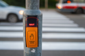 Pressed button for traffic light with wait signal at pedestrian crossing where a car and a bus are passing.