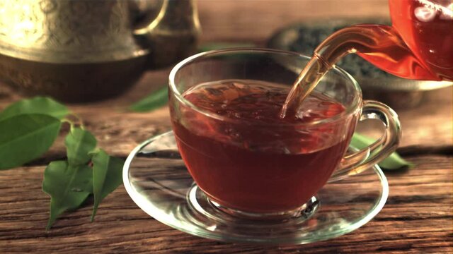 Super slow motion in the cup pour fragrant tea. On a wooden background. Filmed on a high-speed camera at 1000 fps.