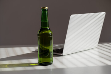 Beer bottle and laptop on white table.