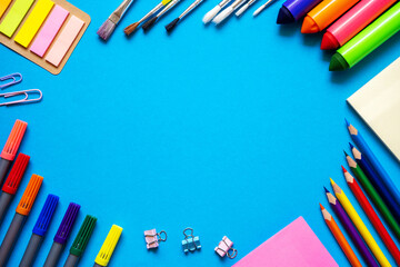 Fototapeta premium Frame from school office supplies. Colorful pencils, felt-tip pens, brushes, stickers and stationery flat lay on blue background. Back to school concept.