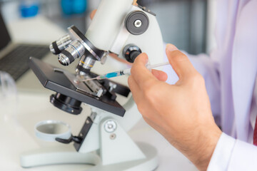 Close up: scientist woman analyzing covid 19 sample with microscope and holding coronavirus covid 19 blood sample tube on hand in laboratory, coronavirus covid 19 vaccine research