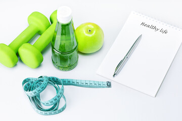 Healthy life written in a white notebook near the apple, bottle of juice and sport equipment on a white table. Healthy life style food fitness concept - Powered by Adobe