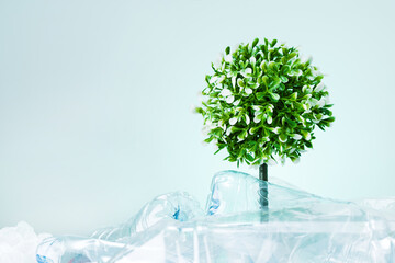 A tree growing from dump of bottles plastic on mint colored background with copy space. Save the earth ecology concept.