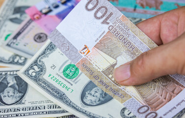 Male hand hold100 Sudanese pounds banknote with US dollars, the currency of Sudan. Close up Paper Money of the arabic country with high inflation. Old man hands shows money. Hand with money, 