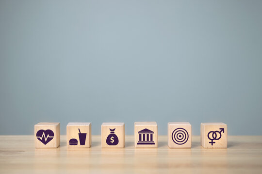 Wooden block arrangement with icons, money, education, health, housing, sex, food, basic human needs concept.