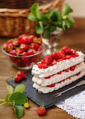 Pavlova dessert with strawberries and violet flowers as a decor on a wooden background