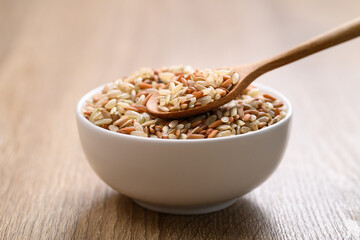 Organic Thai highland brown rice grain in a spoon and bowl on wooden table (Cargo rice, Loonzain rice or Husked rice), Healthy food