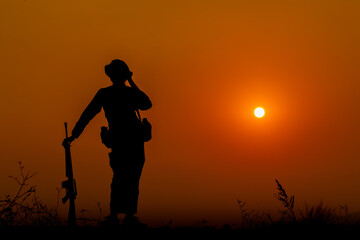 Obraz premium The military silhouettes of soldiers hold gun against with sunset sky background.