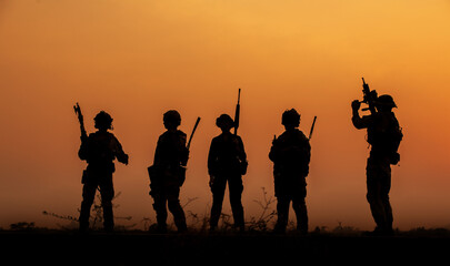 Fototapeta na wymiar The military silhouettes of soldiers hold gun against with sunset sky background