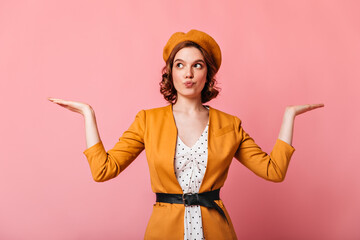 Charming french young woman showing shrug gesture. Studio shot of caucasian girl in yellow clothes posing with hands up.