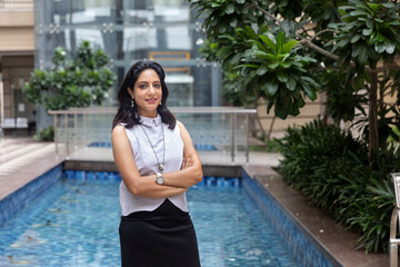 An Indian woman standing with her arms crossed in an urban corporate setting. Corporate female in smart formal attire