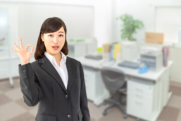 オフィスでOKサインをするカメラ目線のスーツを着た若い女性