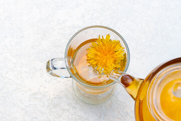 Pouring herbal dandelion tea into a transparent cup from a teapot on a white background, copy...