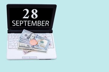Obraz premium Laptop with the date of 28 september and cryptocurrency Bitcoin, dollars on a blue background. Buy or sell cryptocurrency. Stock market concept.