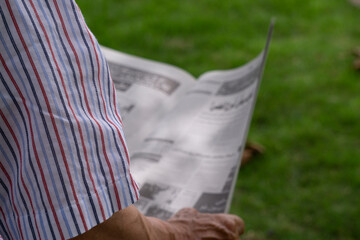 Middle-aged and older or elderly reading a newspaper on a park bench....