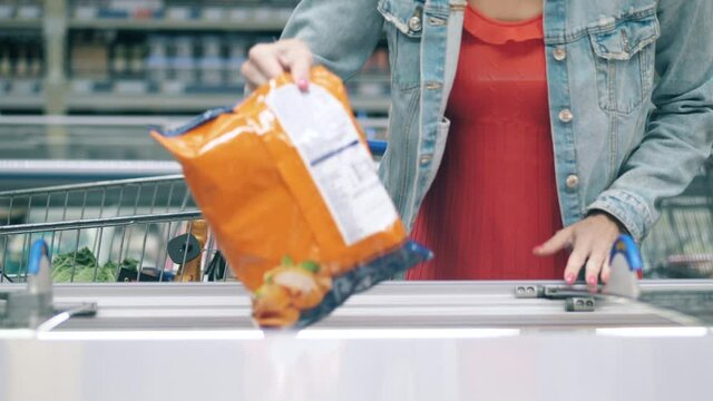 A woman is putting frozen food into a supermarket trolley