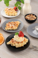 Delicious Homemade Croissant Waffle with Cream, Maple Syrup, Chopped Almond, and Strawberry. Served on Black Plate, Brown Background.