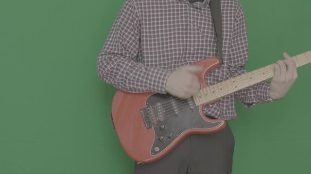 A man in a plaid shirt plays a red electric guitar on a Green Screen, Chroma Key. V-log.