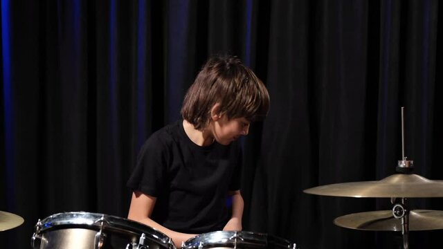 The boy learns to play the drums in the studio on a black background. Music school student