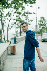middle-aged man walks on city street. portrait of young man with dark but already partially gray hair in blue hoodie near the sea. urban style content. selective focus