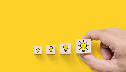 Concept creative idea and innovation. Hand picked wooden cube block with light bulb icon on yellow...