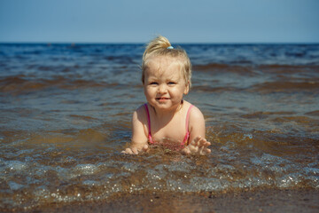 Fototapeta na wymiar Cute Little caucasian blond girl lying in sea in waves. Vacation with kids