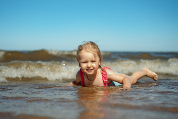 Fototapeta na wymiar Cute Little caucasian blond girl lying in sea in waves. Vacation with kids. Sunny day on the beach
