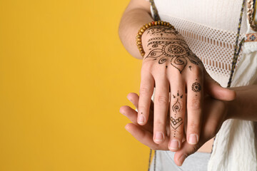Woman with beautiful henna tattoo on hand against yellow background, closeup and space for text....