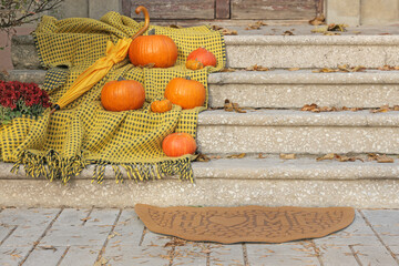 Doormat with plaid, pumpkins and umbrella near entrance of house on autumn day