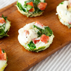 Homemade Egg White Breakfast Cups with Spinach and Tomato on a rustic wooden board, side view. Close-up.