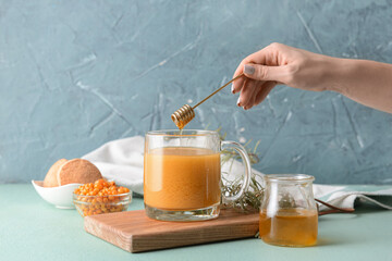 Woman adding honey to healthy sea buckthorn tea in cup