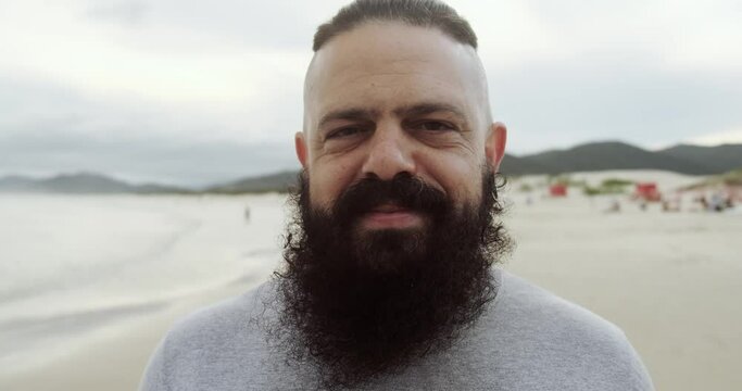 Happy latin man with big beard on a beach looking at camera and smiling. 4K.