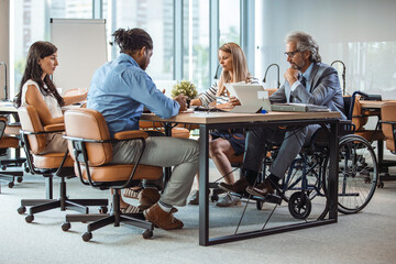 Group of business people in a meeting with colleague in a wheelchair for inclusion. Happy Mature...