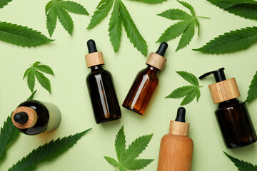 Bottles with cannabis oil and leaves on green background