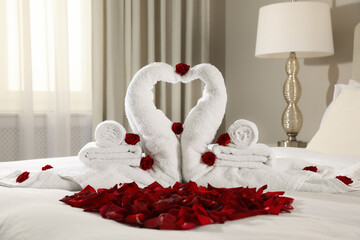 Beautiful swans made of towels and red rose petals on bed in room