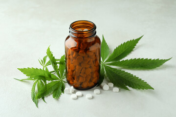 Bottle with pills and cannabis leaves on white textured background