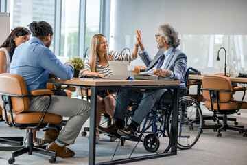 Group of business people in a meeting with colleague in a wheelchair for inclusion. Happy Mature Businessman On Wheelchair With Colleagues In Office.