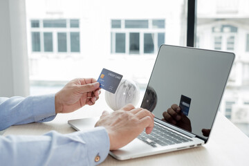 The businessman's hand is holding a credit card and using a laptop for online shopping and internet payment in the office
