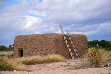 an adobe kiva and ladder on a stormy day at the coronado historic site in bernalilllo, new mexico