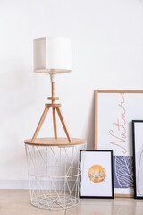 Stylish pictures and table with lamp near light wall