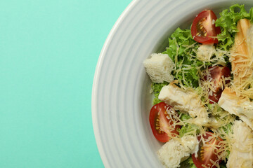 Plate with Caesar salad on mint background
