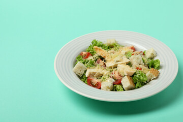 Plate with Caesar salad on mint background