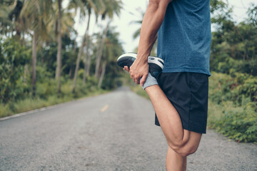 young man stretching in the park before running. Young man workout before fitness training at the park. Healthy and exercise young man warming up on the road in the forest.