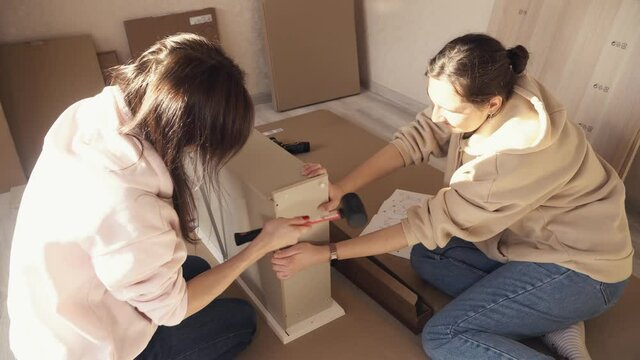 Millennial women doing DIY putting together self-assembly wooden furniture at living room