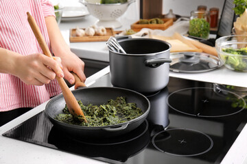 Woman cooking healthy spinach on frying pan in kitchen