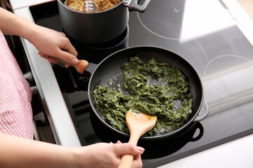 Woman cooking healthy spinach on frying pan in kitchen