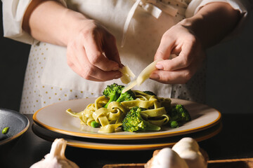 Woman cooking tasty pasta with vegetables and cheese at table