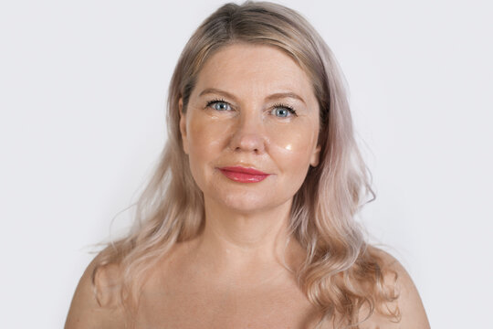 Senior blonde woman is wearing transparent eye patches posing at camera with bare shoulders